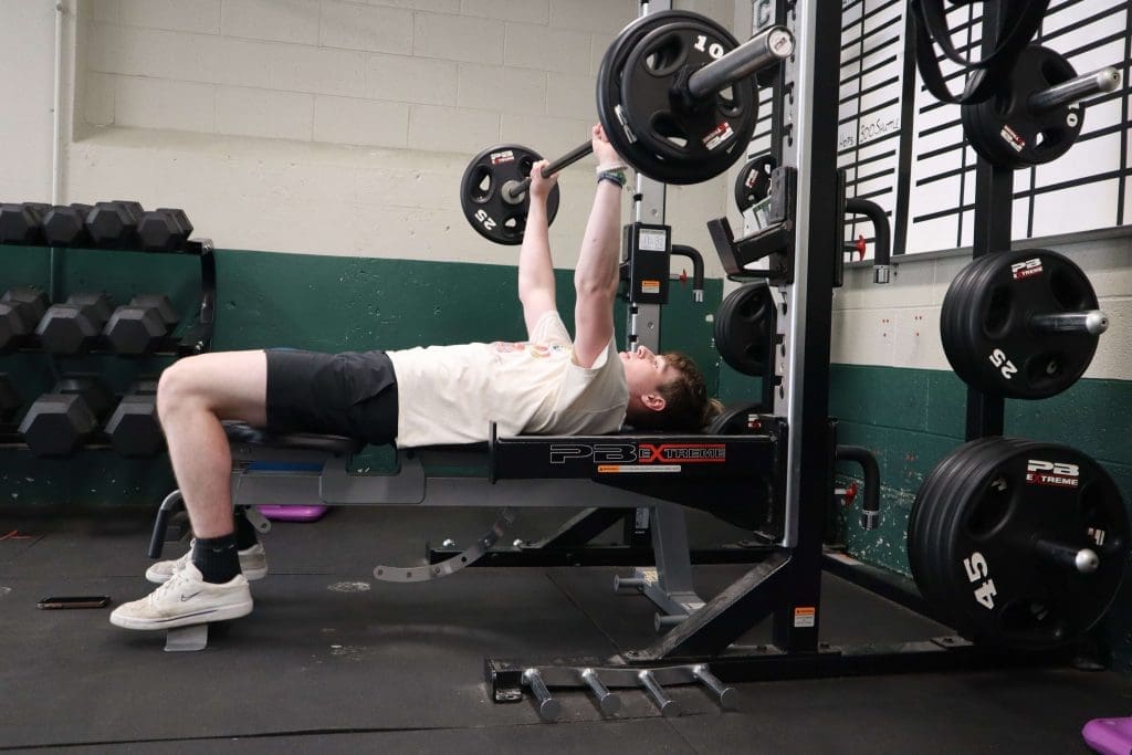 A high school student performs a bench press in the weight room.