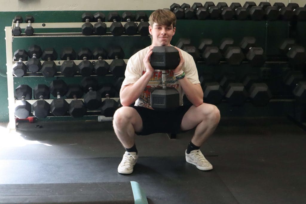 A high school student performs a goblet squat in the weight room.