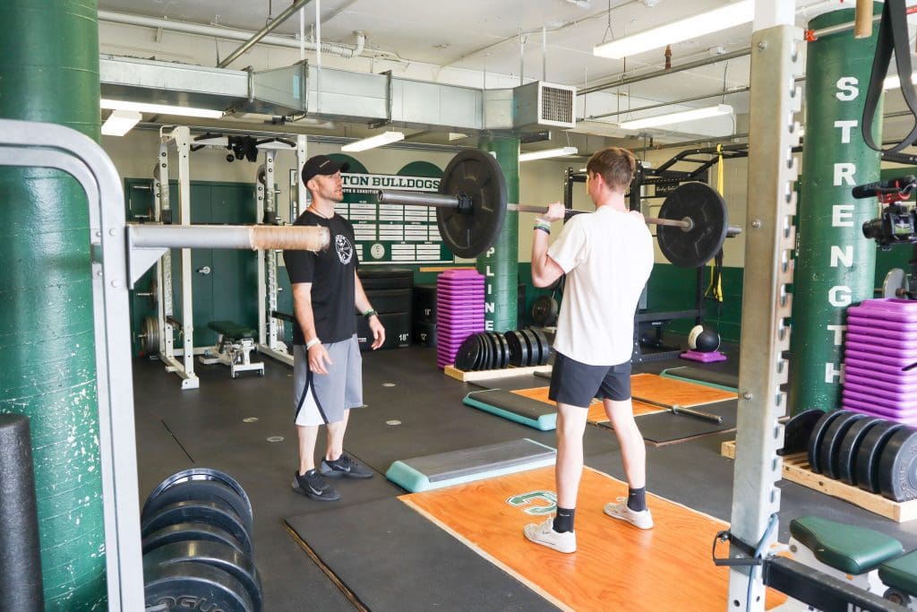 A coach instructs an athlete doing a push press.