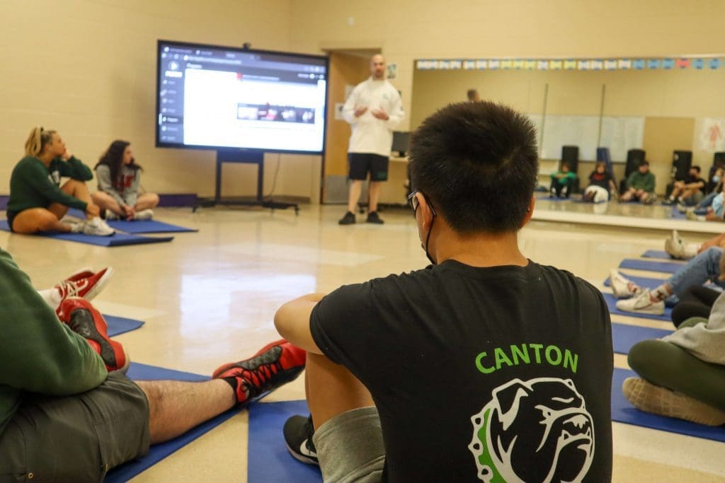 A student listens as a teacher talks about social emotional learning during a yoga lesson in physical education class.