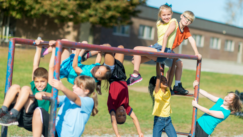 Students hang from a jungle gym on a playground.