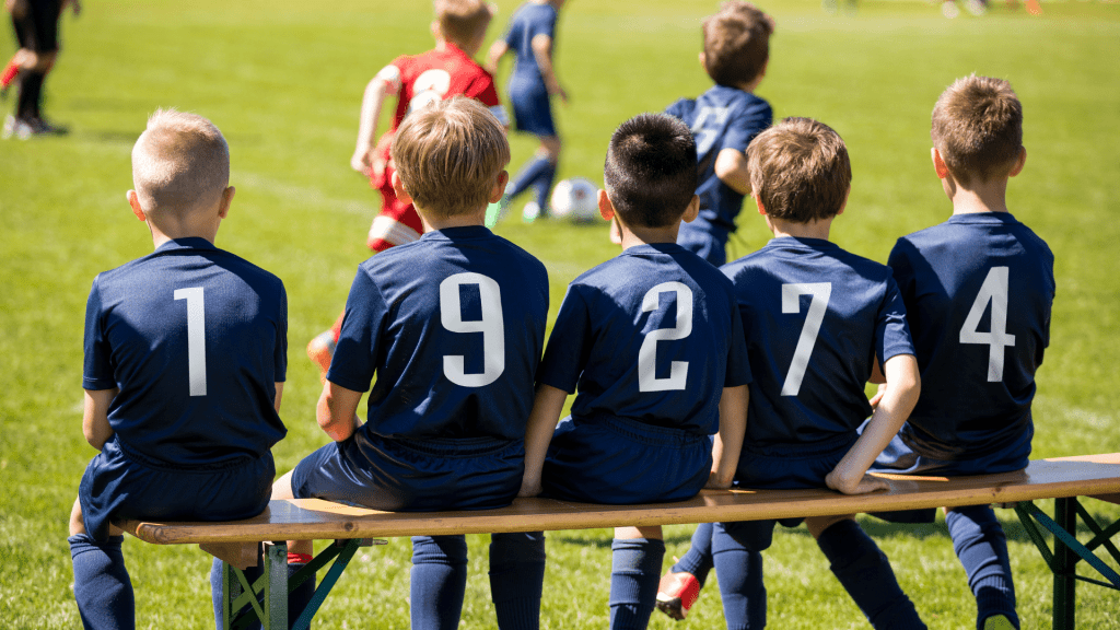 Young boys sit on a bench during a soccer game.