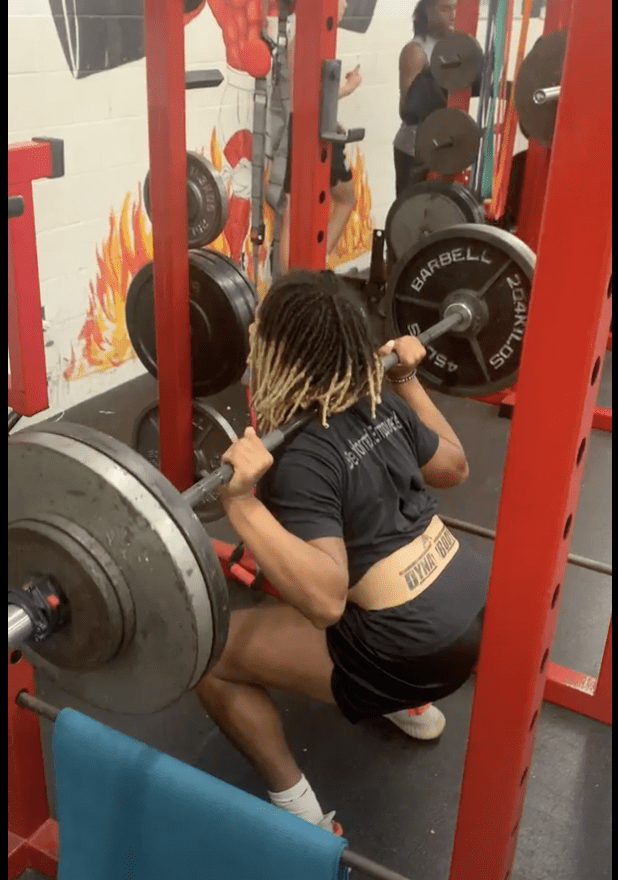 A student performs a barbell back squat in a strength and conditioning physical education class.