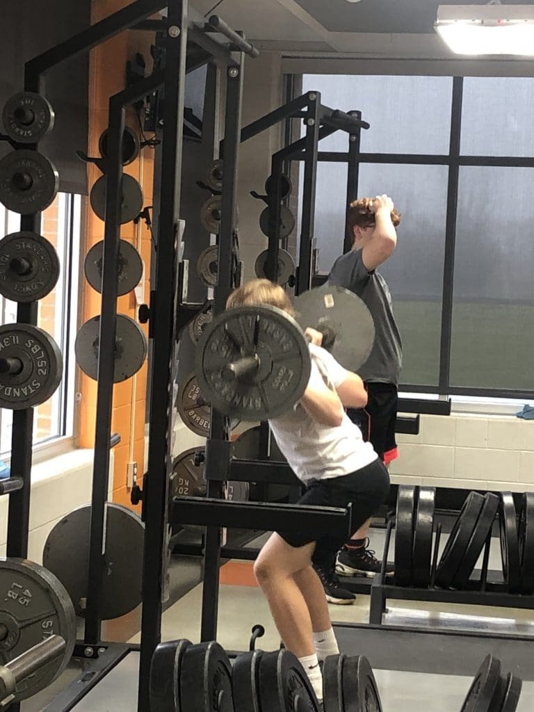 A student performs a barbell back squat rep.