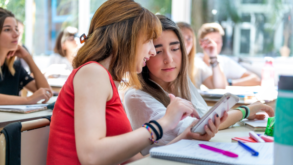 Two students look at a phone in class.