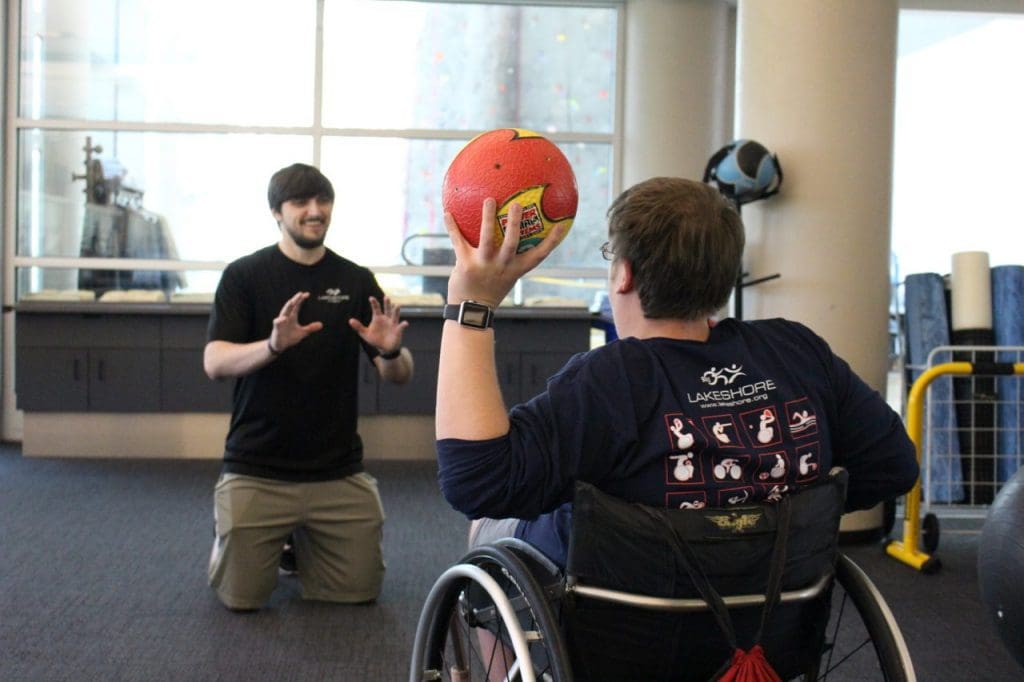 A wheelchair user preparing to throw a medicine ball to his trainer.