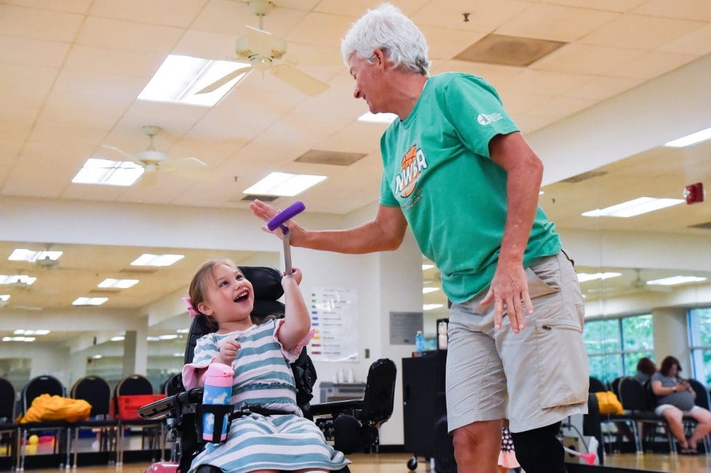 Smiling young girl gives a high five to the instructor from her wheelchair.