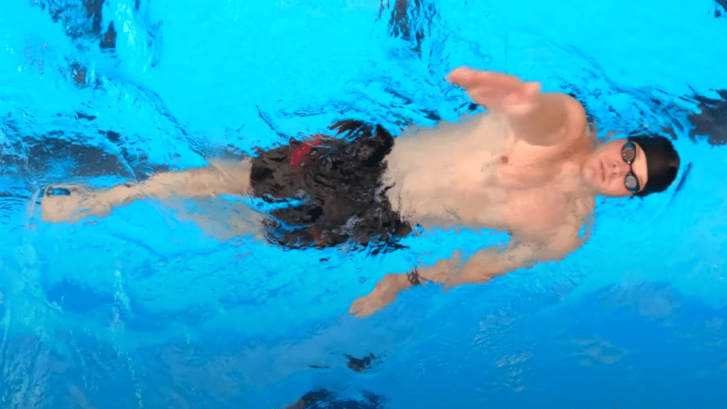 Swimmer performs backstroke, one of the 4 strokes of swimming.