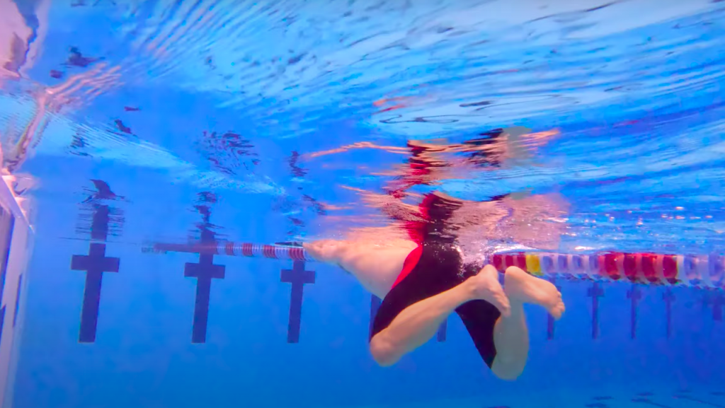 Swimmer prepares to take a breaststroke kick in the water.