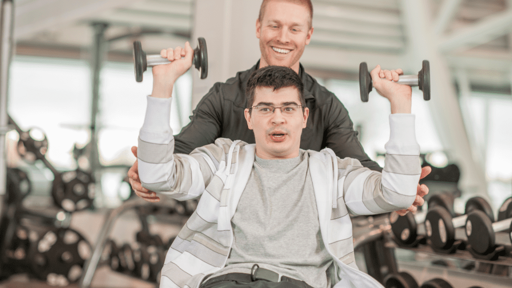 Instructor working with a person in a wheelchair doing overhead press with dumbbells.