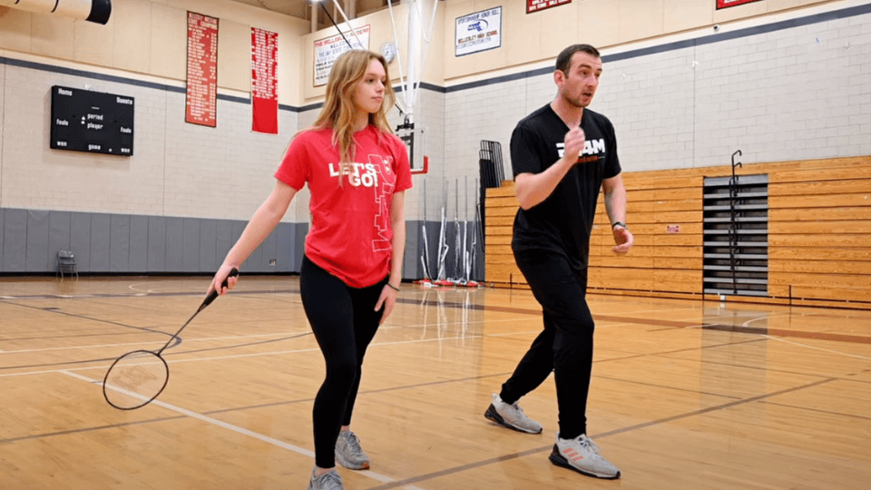 A student practices her badminton skills with a teacher.