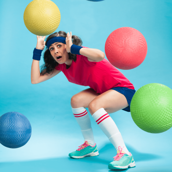 A person in old school gym outfit avoids dodgeballs coming at her.